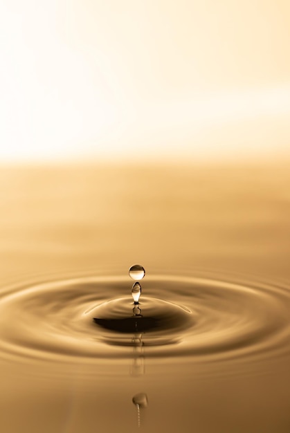 Photo water drop transparent water drop with circular waves slightly blurred golden yellow splattered water droplets natural water drop concept and use it as a background