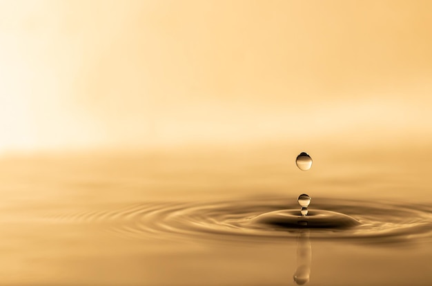 Water drop transparent water drop with circular waves slightly blurred golden yellow splattered water droplets natural water drop concept and use it as a background