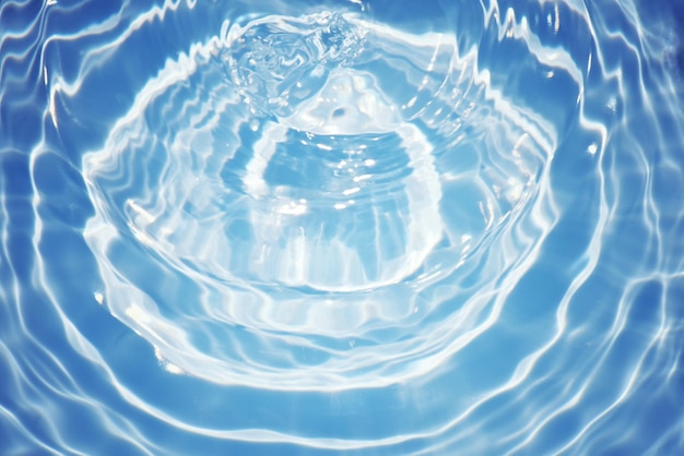 A water droplet is in a blue pool with the sun shining on it.