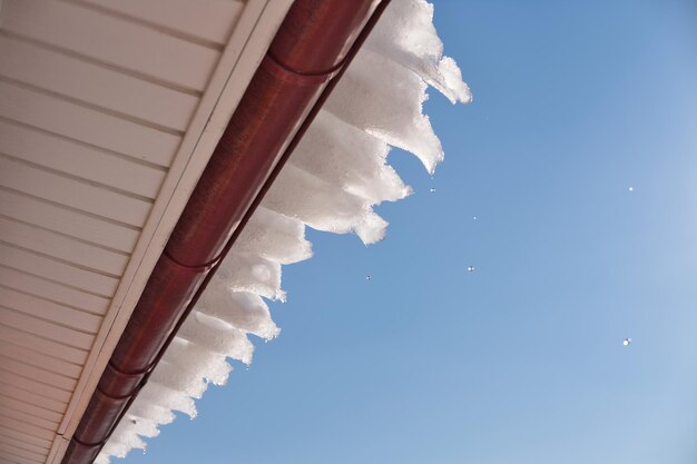 Water droplets falling from the roof against bright blue sky Snow melting in early spring season