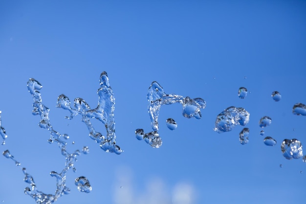 Water droplets frozen in the air with splashes and chain bubbles on a blue isolated background in nature Clear and transparent liquid symbolizing health and nature