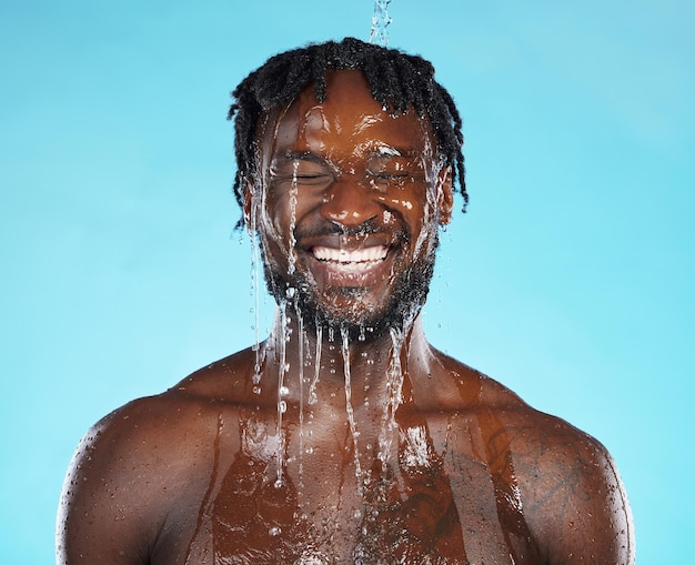 water drops skincare and black man isolated on blue background for face cleaning body shower and smile strong beauty model or person facial glow in studio headshot washing or dermatology hygiene