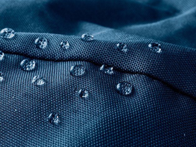 Капли воды на водонепроницаемой мембранной ткани. Детальный вид текстуры синей водонепроницаемой ткани.