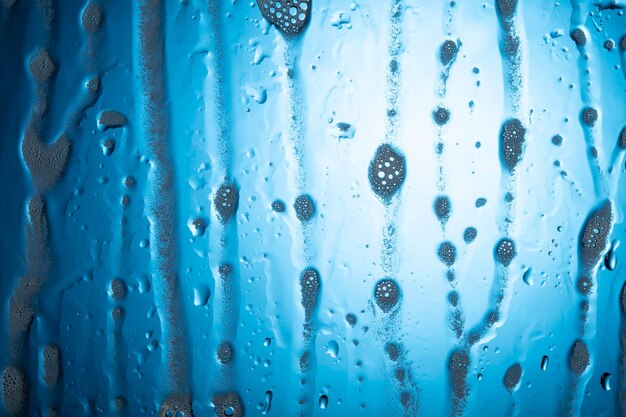 Foto gocce d'acqua con schiuma su vetro su sfondo blu.