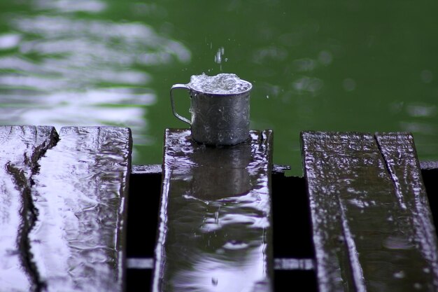 호수 근처 의 나무판 에 금속 컵 으로 떨어지는 물