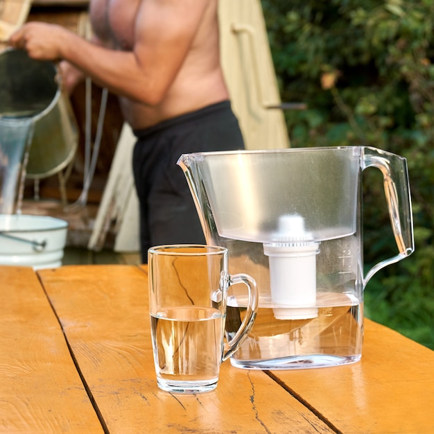 井戸から水を注ぐ上半身裸の少ない男とカップ付き浄水器