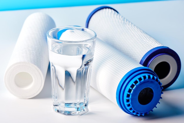 Water filters. Carbon cartridges and a glass on a white background. Household filtration system.