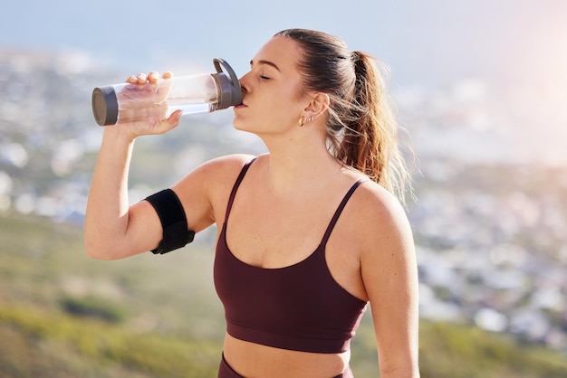 ハイキングのトレーニングの後、フィットネスに水を注ぎ、水を飲み、健康や栄養に挑戦する若いスポーツ選手やランナーの女性で、運動トレーニングや屋外での水分補給のための水筒を持っています