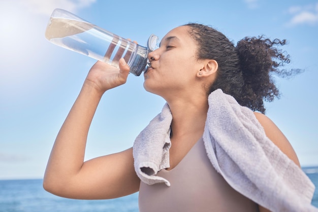 Photo water fitness and woman with a drink after exercise workout or training by the sea sports motivation and energy from a runner with a bottle for hydration after running by the beach in nature