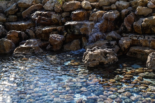 Вода течет по камням в бассейн с камнями на дне