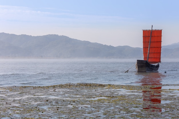 a water fog and a red sailboat.