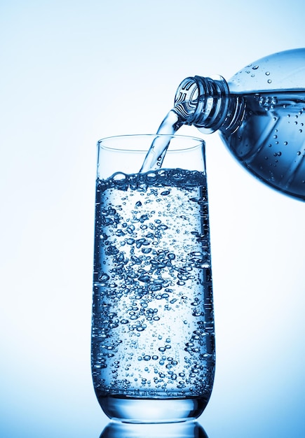 Water gieten in glas uit fles op blauwe achtergrond