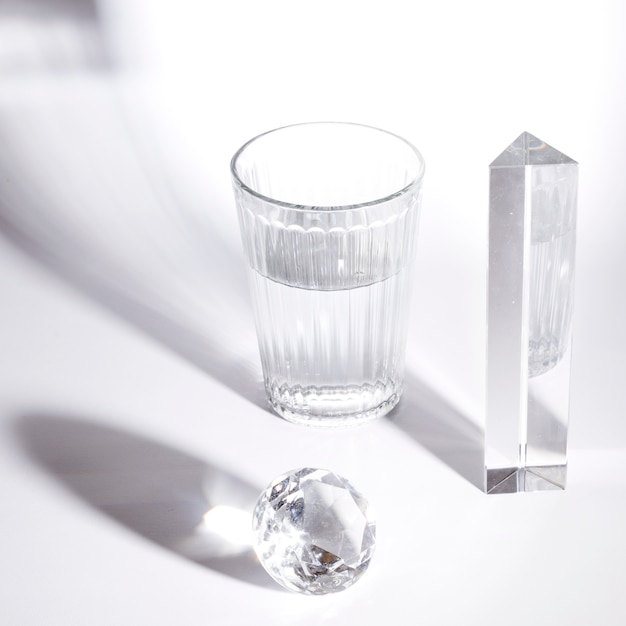 Foto bicchiere d'acqua; diamante di cristallo e prisma con forti ombre su sfondo bianco
