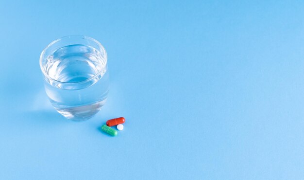 Water glass and tablets on blue background Health and medicine