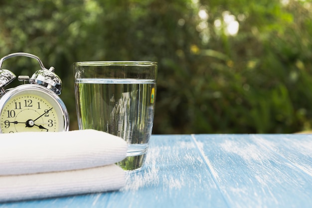 Foto acqua in vetro con sveglia e fazzoletto sullo sfondo della natura.