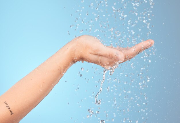 Water hand in shower and cleaning for body wellness and skincare splash and hygiene with hydration against blue studio background Skin body care and water drops clean body and washing palm