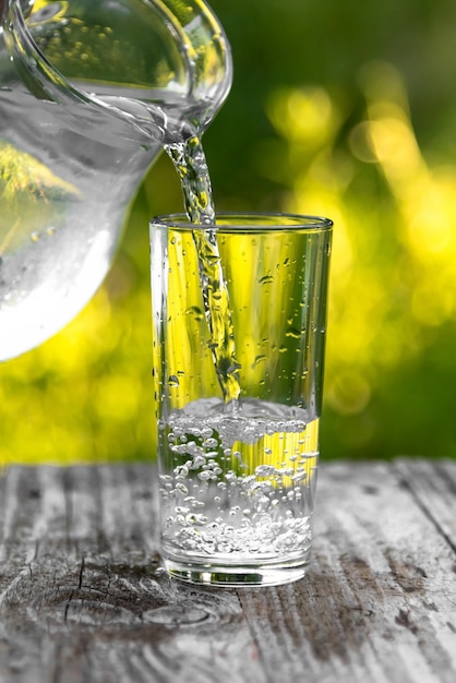 Water is poured into a glass from a jug in the fresh air.