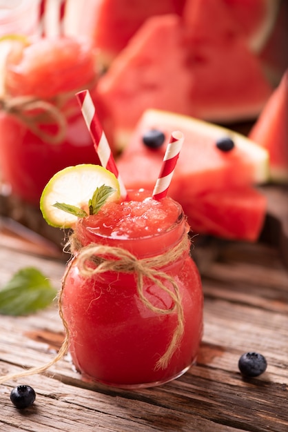 Water melon smoothie garnished with a piece of melon and mint leaves on wooden background