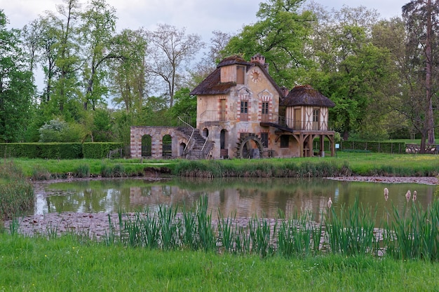 フランスのパリのヴェルサイユ宮殿にあるマリーアントワネットの古い村の水車小屋と湖。