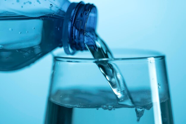 Foto acqua che versa da una bottiglia di plastica in un bicchiere di vetro su sfondo blu