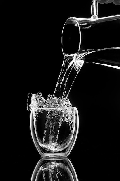 L'acqua versa in un bicchiere da un decanter su sfondo nero