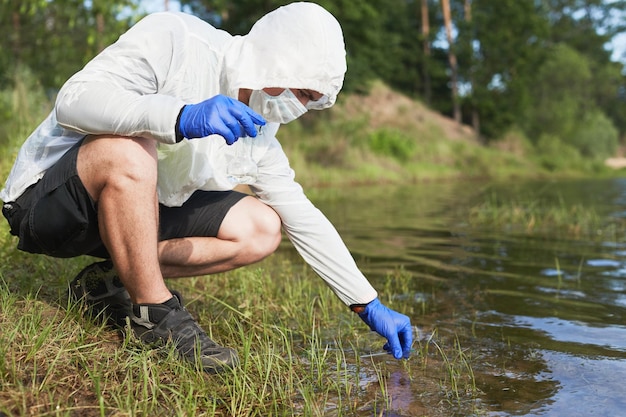 Water purity test hand in protective gloves holding a chemical\
flask or test tube with water lake or river in the background