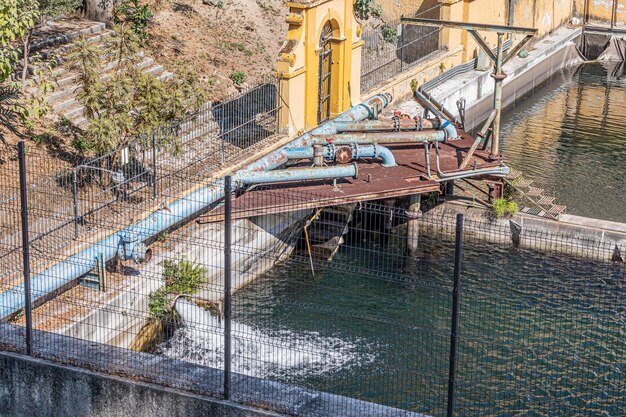 Water reservoir in natural springs of the Colomos forest water flowing in a stream metal fence rusty blue thick pipes yellow weathered walls sunny day in Guadalajara Jalisco Mexico