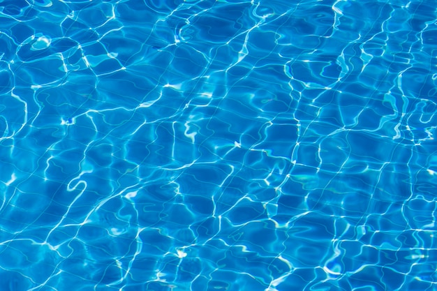 Water ripples on blue tiled swimming pool background. Blue turquoise pool water. Ripples lit up by the sun. Tiles visible below. Top view