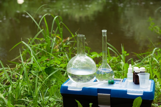 Foto campionamento dell'acqua. una serie di boccette sullo sfondo del fiume. l'assistente di laboratorio preleva campioni d'acqua