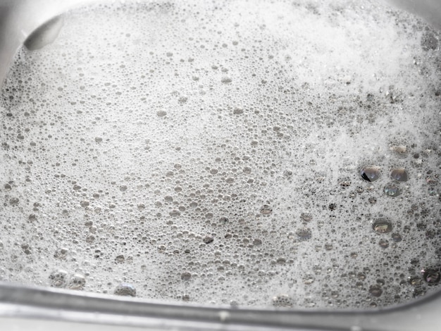 Water and soapy foam after washing dishes in zinc kitchen sink