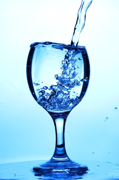 Water spatten in een glas. water gieten in glas op blauwe achtergrond