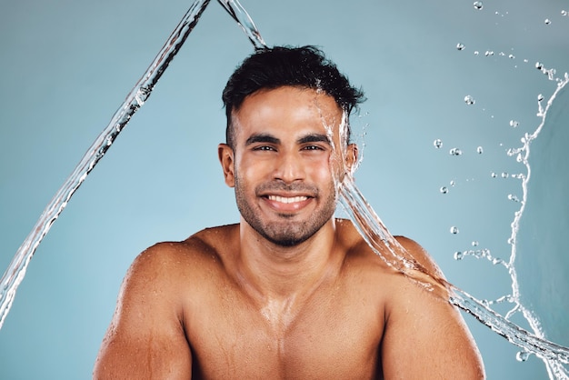 Water splash portrait and skincare man isolated on blue background face cleaning body shower and beauty Fitness model or person in studio headshot for aesthetic washing and dermatology hygiene