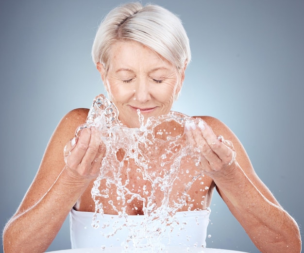 Foto spruzzi d'acqua e donna anziana in studio per la routine cosmetica naturale e facciale per l'igiene salute benessere e signora anziana che fa un trattamento di cura della pelle organico e di bellezza pulito su sfondo grigio