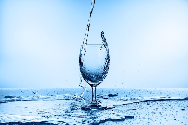 Foto acqua che spruzza dal vetro isolato sull'azzurro