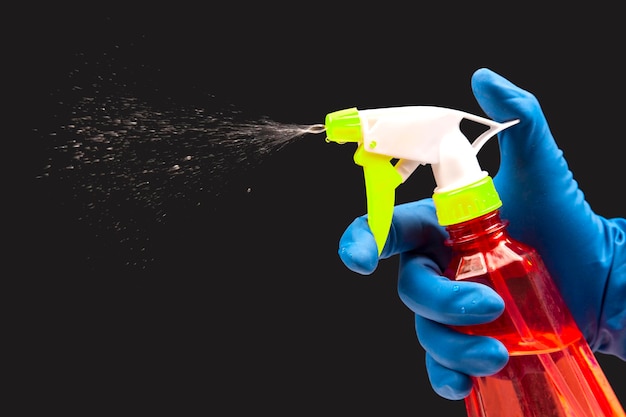Photo water sprayer bottle in a hand in a protective glove spraying liquid on a dark background. household items for home