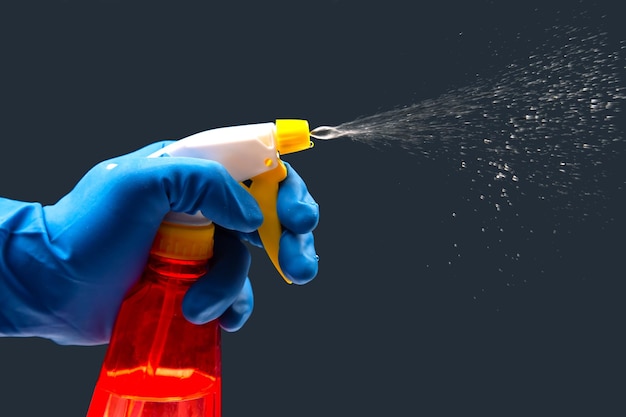 Water sprayer bottle in a hand with gloves on a dark background with liquid spray household items for home