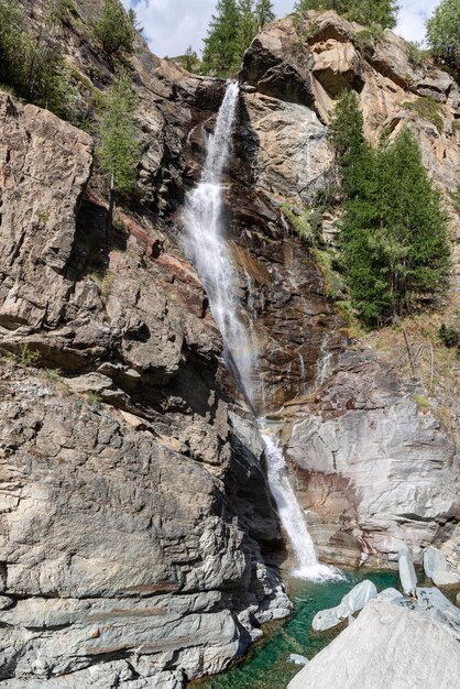 Photo water streams over granite rapids into emerald lake surrounded by trees vertical aosta valley