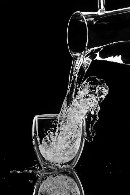 Water stroomt in een glas uit een karaf op zwarte achtergrond