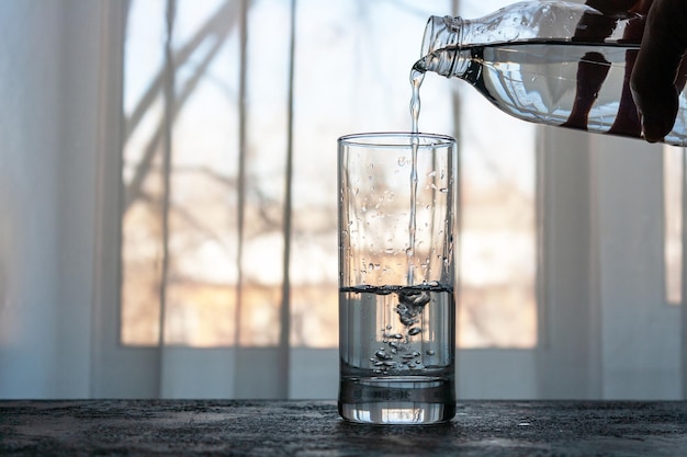 Water stroomt uit een fles in een glas op de achtergrond van het raam