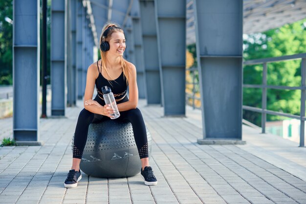 Water time. Woman leading healthy lifestyle drinking water before exercising on fitness ball