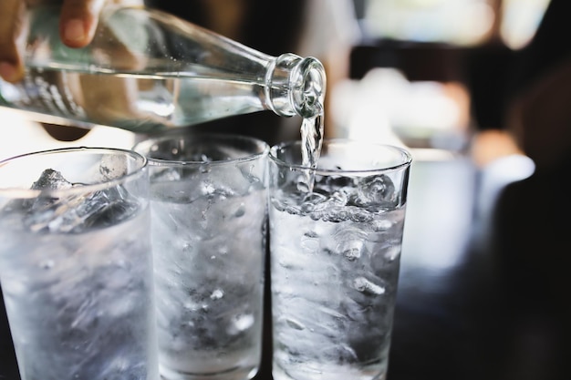 Water uit een fles in een glas gieten met ijsblokjes op tafel