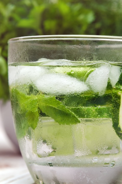 Water with cucumber, mint and ice in glassware on wooden table.