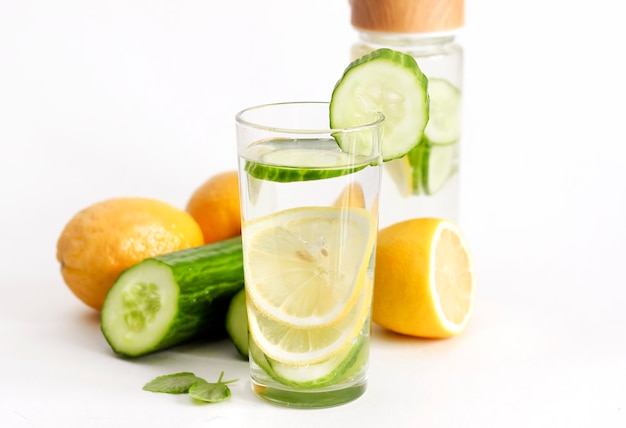 Acqua con limone e cetriolo in bottiglia e bicchiere su sfondo chiaro.