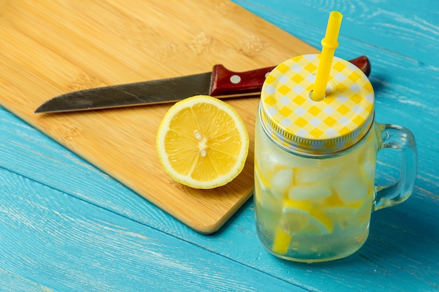 Acqua al limone limonata con fette di limone, vaso con paglia su fondo di legno blu.