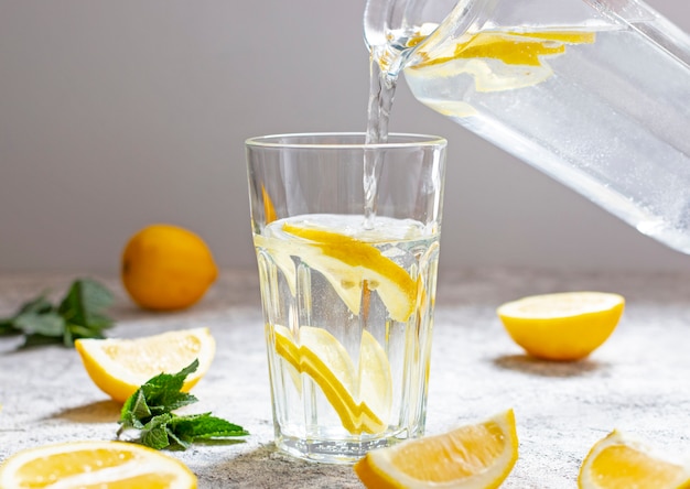 Water with lemon, mint and ice. Water is poured from a glass jug into a glass. Close-up.