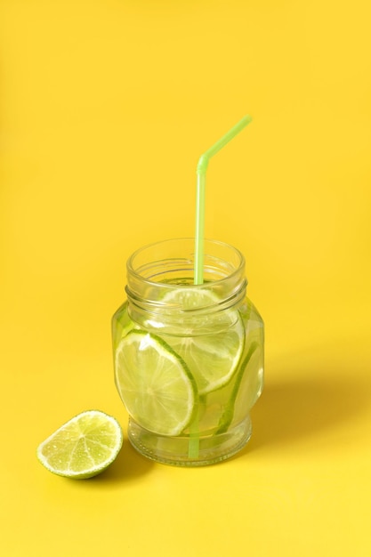 Water with lime slices in a glass jar on a yellow background