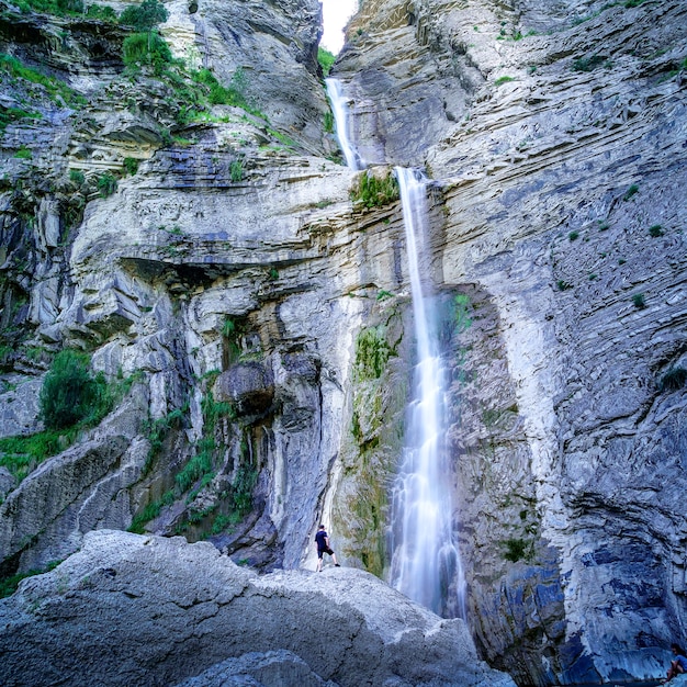 Watercascade op rotsmuur die van grote hoogte valt met persoon die zich op rots bevindt die het water bekijkt. spanje