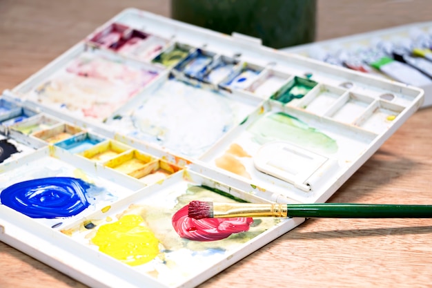 Watercolor paint and brush in white box,palette  on wood table.