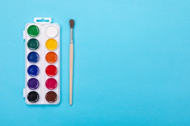 Watercolor paints and brush in white box, isolated on blue 