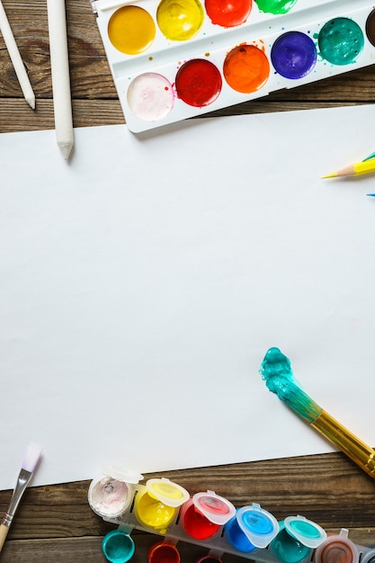 Watercolor Paints and brushes with blank white paper on wooden table